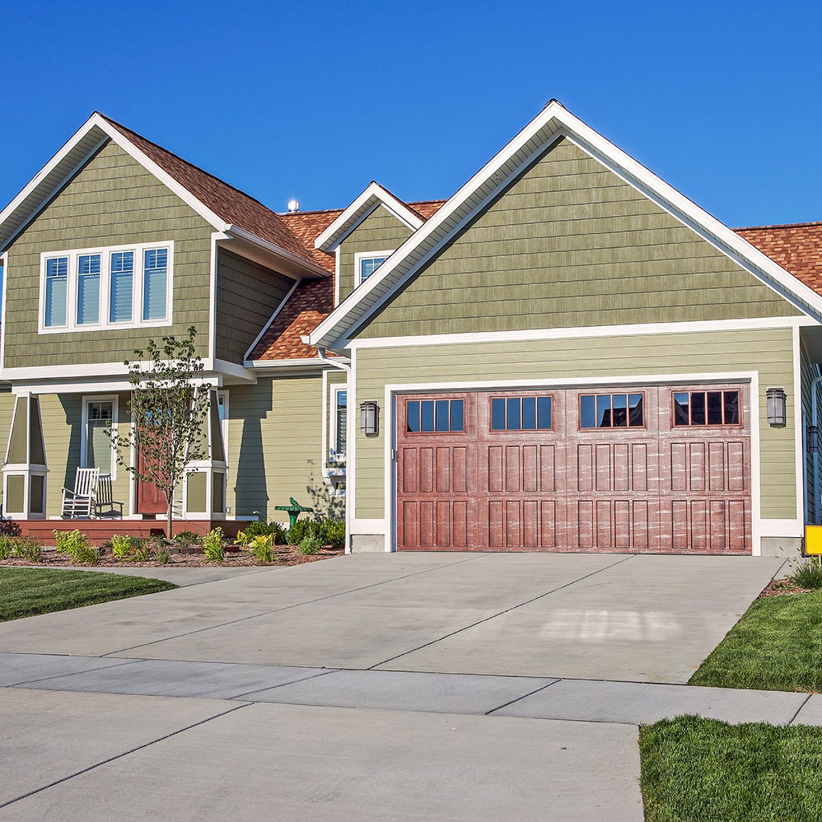 Green two-story home with new siding and a wood-style garage door installed by Shinnova.